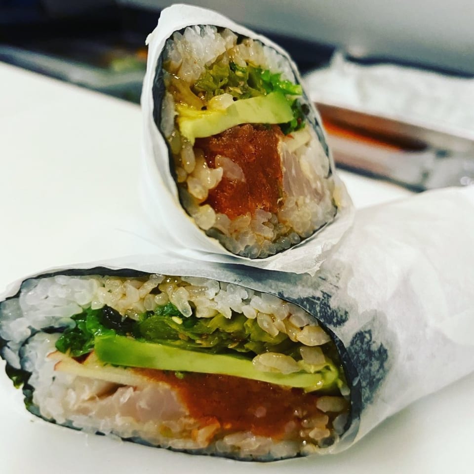 Two sushi burritos, one standing and one lying down, filled with tuna, avocado, and greens.