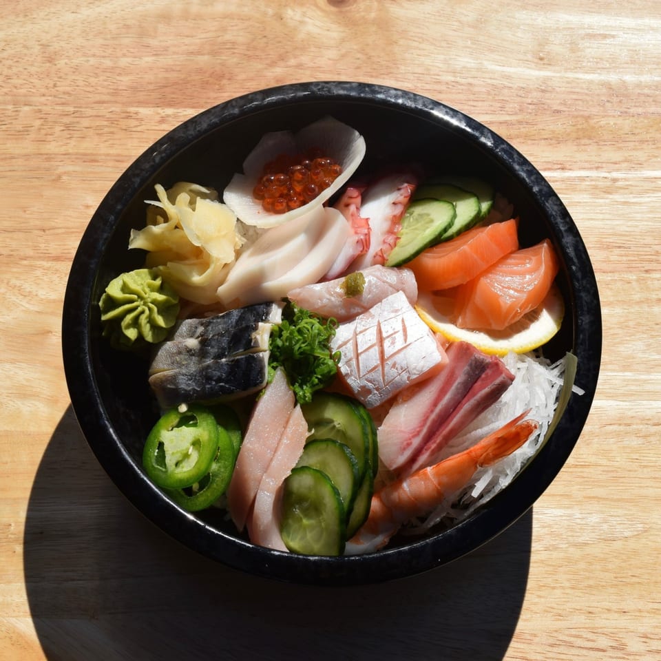Overhead view of a colorful Poke Box Sushi Bar chirashi bowl with various sashimi, roe, and vegetables.