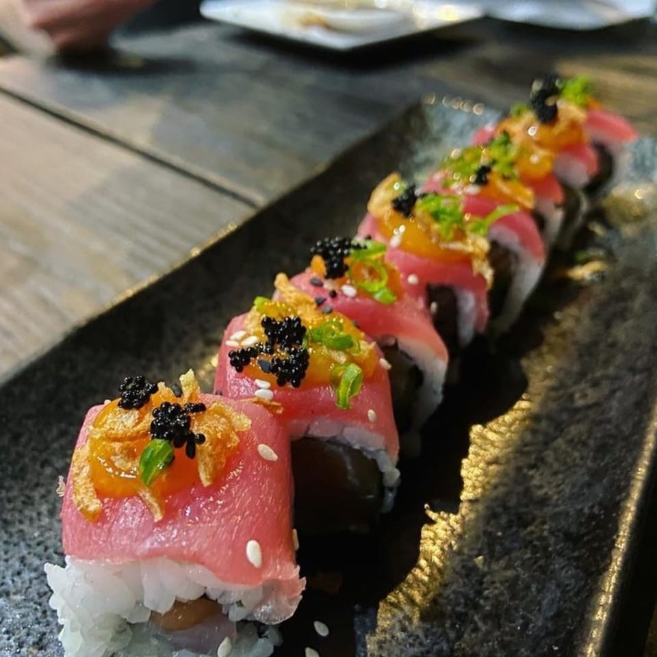 A row of Poke Box Sushi Bar's tuna sushi rolls, topped with caviar, fried onions, and green onions.