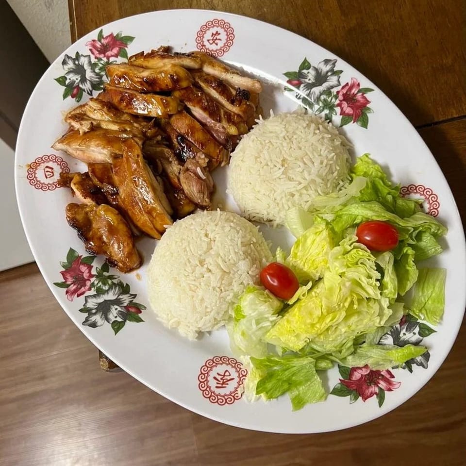 Teriyaki chicken with two scoops of white rice and a side salad with cherry tomatoes.