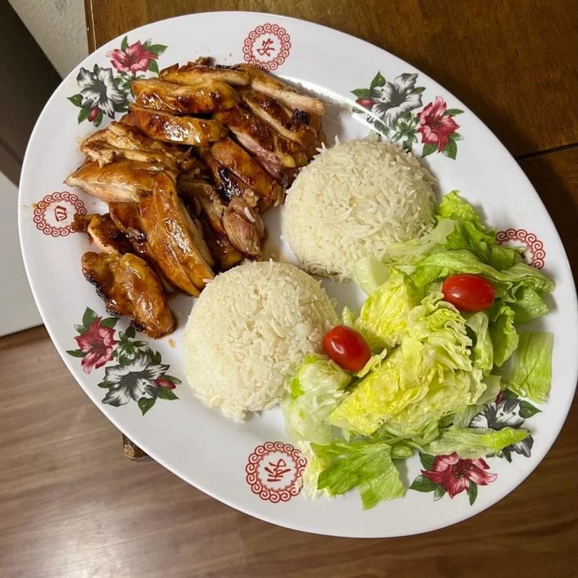 Teriyaki chicken with two scoops of white rice and a side salad with cherry tomatoes.